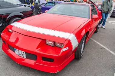 Fords Mustang gibi canlı kırmızı bir spor araba, halka açık bir etkinlikte park edilmiş. Beyaz çizgili ve performans odaklı Kyiv, Ukrayna 10-12-2024