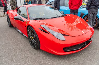 Bir toplantı ya da etkinlik sırasında şehir caddesinde parlak kırmızı bir Ferrari spor arabası park halindedir, yakınındaki izleyiciler güneşli hava durumu Kyiv, Ukrayna 10-12-2024