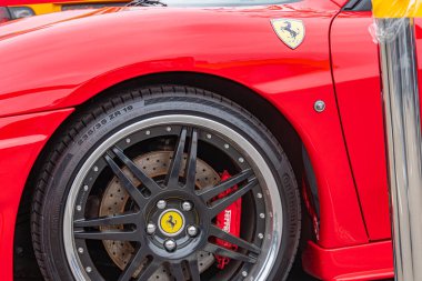 Kırmızı spor bir araba, muhtemelen Ferrari, ön sol tarafta sarı çerçeveli tekerlekler ve havalı at amblemi ile gösteriliyor. Arabanın parlak bir finişi var ve Ukrayna, 10-12-2024