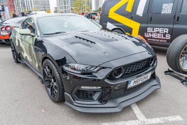 Saldırgan bir stile sahip siyah, modifiye edilmiş bir Ford Mustang bir etkinliğe ya da toplanmaya park edilir. Arabanın özel bir vücut kiti, büyük bir arka kanat spoiler 'ı, kaputta havalandırma delikleri ve Kyiv, Ukrayna 10-12-2024