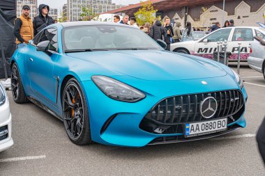 Bir açık hava etkinliğinde parlak mavi bir Mercedes-Benz AMG GT, muhtemelen bir sergi veya otomobil fuarı. Kişisel siyah tekerlekleri olan araba, t Kyiv, Ukrayna 10-12-2024 'ün ayırt edici tasarımını içeriyor.