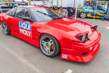 Geniş gövdeli, aerodinamik modifikasyonları olan kırmızı bir yarış arabası ve Liquid Moly gibi sponsor logoları şehir yarış ortamında bir açıyla konumlandırılmıştır. Kyiv, Ukrayna 10-12-2024