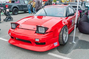 Aerodinamik özelliklere sahip canlı kırmızı bir spor araba, halka açık bir etkinliğe veya toplantıya park edilmiş, 15 ve RJ Racing numaralı çıkartmaları var. Arka plan Kyiv, Ukrayna 10-12-2024 insanlarla dolu.