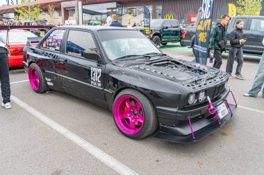 Pembe aksanlı, modifiye edilmiş siyah bir araba bir araba etkinliğinde ya da toplanırken Ukrayna, 10-12-2024 'te Kyiv' de arabanın fotoğrafını çeken iki kişiyi görüntüler.