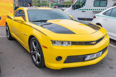 Siyah aksanlı, parlak sarı bir Chevrolet Corvette, asfaltlı bir yüzeye park edilmiş. Arabanın yan şeridi, renkli aynaları, siyah hava delikleri, çok dilli tekerlekleri, bir Kyiv, Ukrayna 10-12-2024