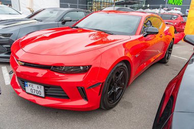 Kırmızı bir Chevrolet Camaro spor arabası kapalı otoparkta park halinde, parlak tasarımını ve belirgin hava girişlerini sergiliyor. Arka planda Kyiv, Ukrayna 10-12-2024