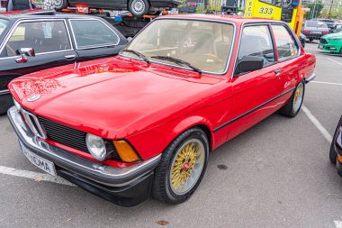 Canlı kırmızı renkli bir BMW, belirgin kıvrımlı kapüşonlu ve spor kepçeli, halka açık bir otoparkta veya araba fuarında park halinde. Araç iyi korunmuş, Kyiv, Ukrayna 10-12-2024