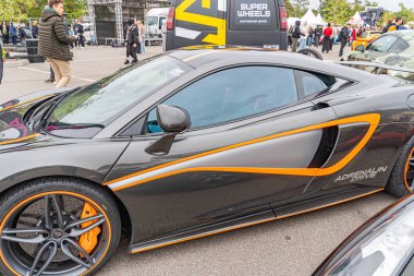 Siyah ve turuncu yüksek performanslı bir Aston Martin halka açık bir etkinlik sırasında bir caddede park halinde. Görüntü araba tasarım özellikleri ve Kyiv, Ukrayna 10-12-2024 markasını yakalıyor.