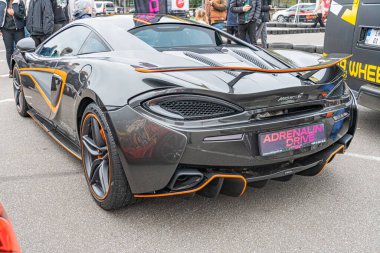 Turuncu aksanlı siyah bir McLaren 675 LT spor arabası, muhtemelen yağmurdan sonra ya da ışığı yansıtan ıslak bir alana park edilmiştir.