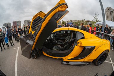 Bir otomobil fuarında, savaş uçağı tepe örtüsüne benzeyen alışılmadık bir kapı yapısına sahip sarı bir spor araba sergilenmektedir. Görüntü dinamik atmosfer tipi Kyiv, Ukrayna 10-12-2024 'ü yakalar.