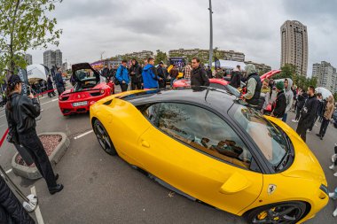 Parlak sarı bir Ferrari ve muhtemelen başka bir yarış arabası da dahil olmak üzere spor arabaların etrafında toplanan kalabalık, kentsel bir çevrede insanlar fotoğraf çekiyor ve hatta Kyiv, Ukrayna 10-12-2024