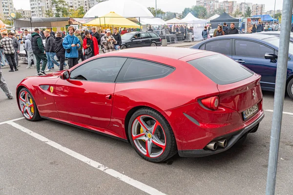 Canlı kırmızı bir spor araba gündüz vakti bir caddeye park edilir parlak tasarım ve renkli camlar dikkatleri çekerken, yakınlarda bir kalabalık toplanır görüntü düz bir Kyiv, Ukrayna 10-12-2024