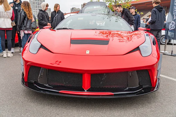 Görüntü, yüksek performanslı, açık hava otomobil etkinliklerinde park edilmiş, parlak kırmızı bir spor araba tasvir ediyor veya 10-12-2024 Ukrayna 'nın taşralı Kyiv kentinden izleyicilerin günlük kıyafetlerini gösteriyor