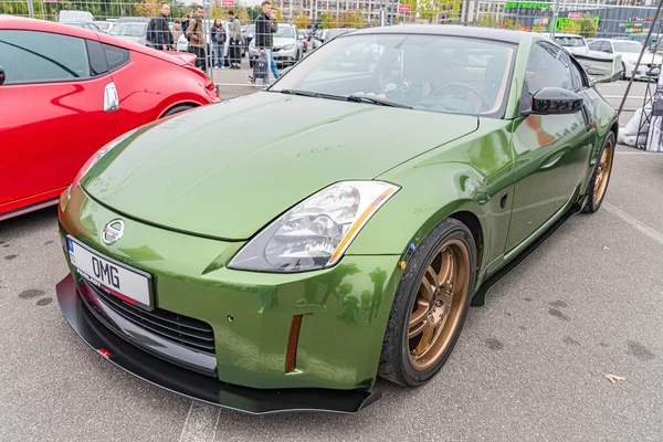 Canlı yeşil bir Nissan Skyline GT-R R34 arabası, aerodinamik kıvrımlar ve deliklerle halka açık bir etkinlikte park edilmiş durumda. Görüntü ayrıca Ukrayna, Kyiv 'deki diğer arabaları da içeriyor.