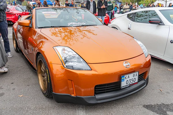Özel yapım Nissan Skyline spor arabası bir etkinlikte sergilenirken, arkasında ziyaretçi kalabalığı bulunan araç altın aksanlı turuncu renkte ve sonrasında piyasa güncellemeleri Li Kyiv, Ukrayna 10-12-2024