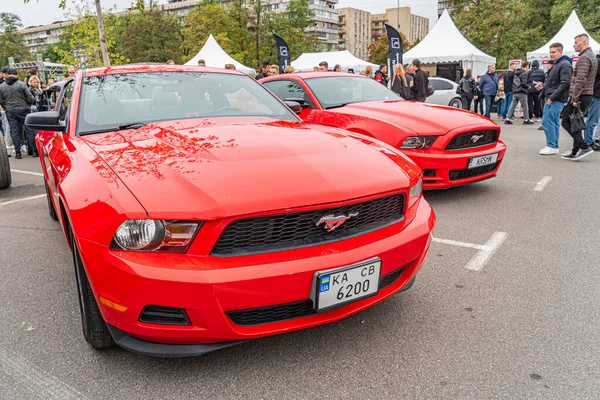 Açık hava araba fuarı sahnesinde iki adet klasik Amerikan kaslı arabası, muhtemelen bir Pontiac GTO ya da Mustang People, Ukrayna, Kyiv 'de 10-12-2024 numaralı çadırda kurulmuş satıcılar olarak günlük kıyafet imalathanesinde.