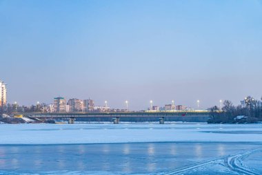 Kyiv nehrinin donmuş yüzeyi, arka planda kentsel ufuk çizgisi, beyaz ve mavi baskın renk paleti, gri ve kahverengi bina ipuçları, yumuşak lig Kyiv, Ukrayna - 23 Şubat 2025