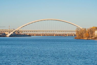 Dinyeper Nehri ile Kiev manzarası, su ile yayılan metal kemerli köprü, ince yansıma, kıyılarda sonbahar yaprakları, arka planda kentsel gelişim, iki köprü Kyiv, Ukrayna - 19 Ocak 2025