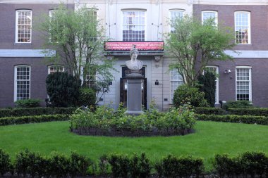 Girişin üzerinde yeşil çalılar ve ağaçlarla çevrili tarihi bir binanın önünde iyi korunmuş bir bahçe.