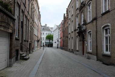 Tarihi tuğla binalarla dolu sessiz bir kaldırım taşı caddesi, mimari tarzların karışımı, arka planda yeşillik var.