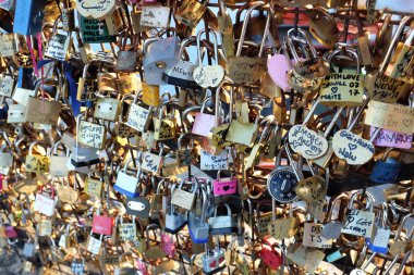 Çite iliştirilmiş sayısız asma kilidin yakın bir görüntüsü, her birinin eşsiz oymaları ve renkleri var, aşkı ve bağlılığı simgeliyor.