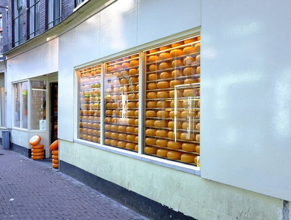 A shop window displaying rows of round orange cheeses, with a street view in front