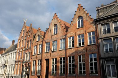 Bulutlu bir gökyüzünün altında şehir meydanında çatıları olan tarihi tuğla binalar.