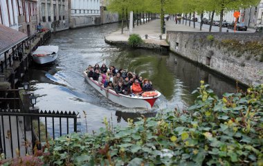 Bir grup insan, yeşil ve tarihi binalarla çevrili bir kanalda tekne turunun keyfini çıkarıyorlar.
