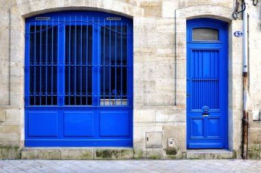 Dekoratif parmaklıklı ve uyumlu kapılı bir pencerenin dokulu taş bir duvara dayandığı canlı mavi bir cephe.
