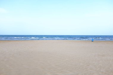 Sakin bir kumsal sahnesi Yumuşak kum ve yumuşak dalgalar altında berrak mavi bir gökyüzü