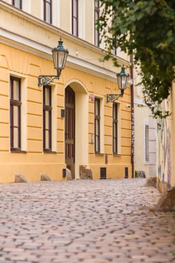 Prag, Çek Cumhuriyeti - 15 Mart 2026: Sarı cephe, sokak lambaları ve geleneksel kaldırım taşları olan dar bir sokağa dikey bakış.