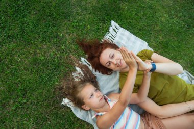 İki neşeli insan yemyeşil çimenlerin üzerine yayılmış yumuşak bir battaniyenin üzerinde uzanır. Neşeli bir el oyununa katılan kahkahalar güneşin altında sıcak havayı doldurur..