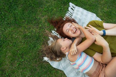 Bir anne ve kızı, yeşil bir parkta battaniyeye uzanmış sıcak güneşin altında birlikte vakit geçirirken neşe dolu bir kahkahayı paylaşıyor ve sürekli mutluluk anıları yaratıyorlar..