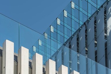 Beton sütunlu modern cam cephe ve arka planda berrak mavi gökyüzü.