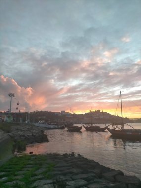 Portekiz 'in Porto şehrinde gün batımı, Douro nehrinde köprüler, bulutlar ve tarihi binalarla.