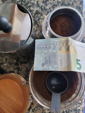 Geleneksel bir İtalyan espresso makinesini ve kahve çekirdeklerini 5 avroluk banknotla kapatın, ev bütçesini, tasarruf parasını ve Avrupa 'da kafeinin fiyatını betimleyin..