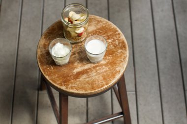 Yulaf gevreği, muz ve elma, cam bir kavanozda. Müsli'ye yoğurt ve süt, faydalı bir kahvaltı, kahvaltıda lezzetli, kahveden tahta küçük bir masada kahvaltı.