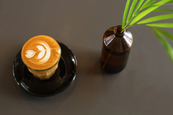 Mug of hot latte, tasty latte, a bottle glass with a flower, a gray background, — Stock Photo, Image