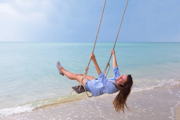 Summer solar portrait of fashion of a way of life of the young stylish woman,sitting on a swing on the beach,carrying lovely fashionable, to requirements of travel, the smile possesses her days off — Stock Photo, Image