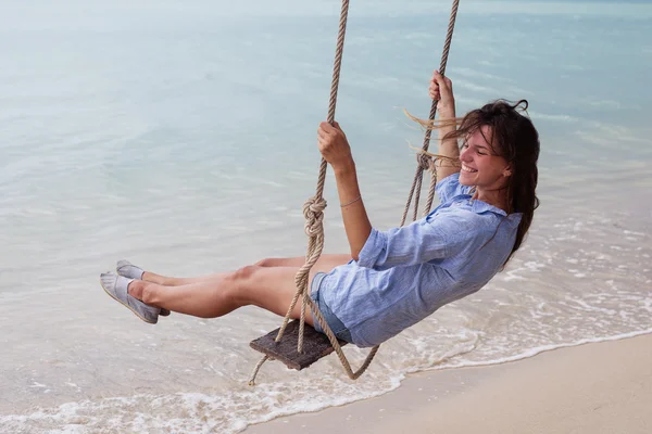 Plajda salıncakta sallanan genç bir kadının moda tarzının yaz portresi seyahat gereksinimlerine karşı, gülümsemesi izin günlerini ele geçirir. — Stok fotoğraf