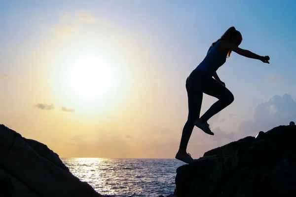 A fiatal gyönyörű lány a sportswoman, a Sportruházat cipők ugrik át sziklák naplementekor, egy nagy ugrás, testedzés, fitness az oktató, extrém sport, Parkour, — Stock Fotó