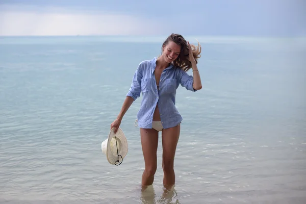 La bella ragazza con un cappello su una sega, sulla spiaggia tropicale, con un sorriso sul viso — Foto Stock