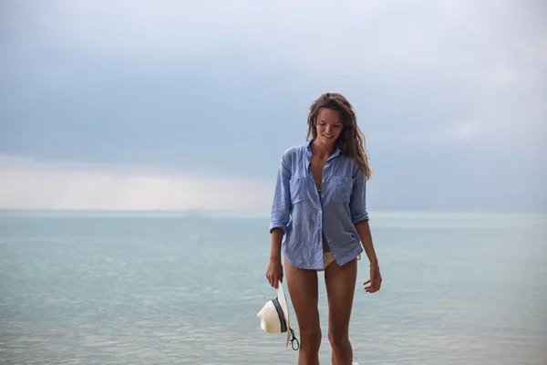 La bella ragazza con un cappello su una sega, sulla spiaggia tropicale, con un sorriso sul viso — Foto Stock