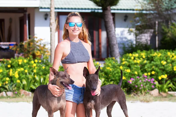 Vacker i jeansshorts och en undertröja flickan också gatsya med hundar, spel med hundar på stranden — Stockfoto