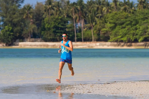 The man runs, runs on the beach, in the tropical country plays sports