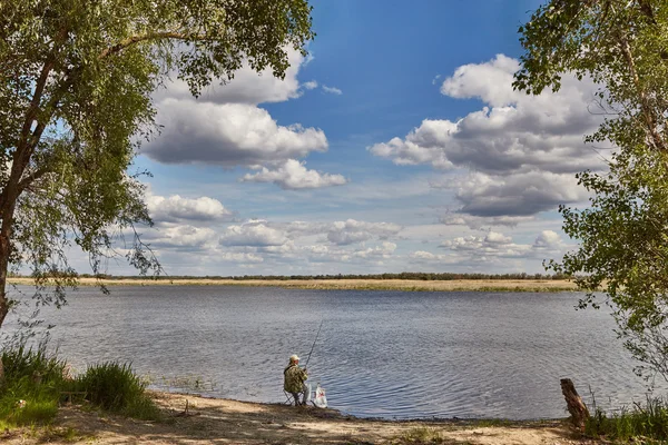 Moln över floden och fiskaren med ett spö — Stockfoto