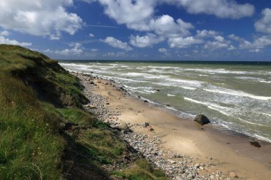 Deniz manzaralı manzara fotoğrafı, Kuzey Denizi dalgaları ve yeşil tepeler Danimarka 'da Hirtshals yakınlarında bulutlu mavi bir gökyüzüne karşı.