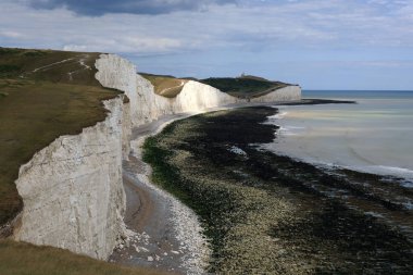 Seven Sisters tebeşir kayalıklarının panoramik manzara fotoğrafı, kısmen güneş tarafından aydınlatılmış, ve İngiltere, Eastbourne yakınlarında bulutlu bir gökyüzüne karşı İngiliz Kanalı kıyı şeridi