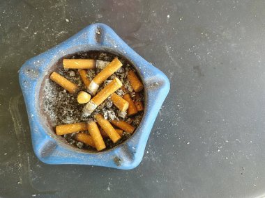 Masadaki kül tablasında sigara izmariti yığını var..