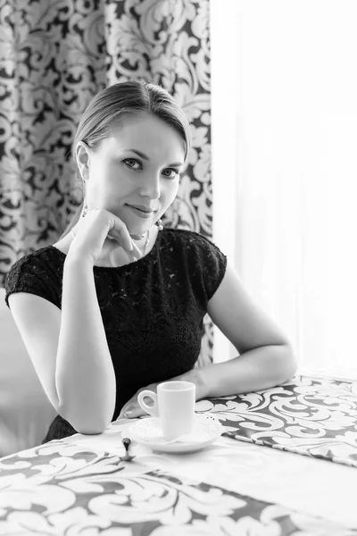Jonge mooie vrouw in zwarte klassieke jurk met lang donker haar in een caffe koffie drinken in de ochtend. BW foto — Stockfoto